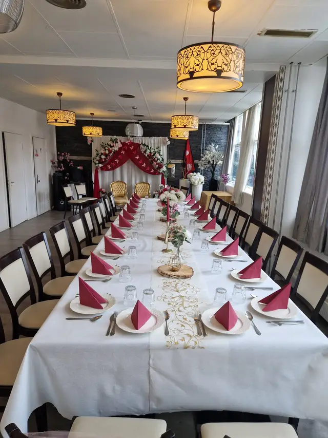 The hall seen down one long table of raspberry napkins to a red draped backdrop with butterflies, two gilded chairs and lamps lit