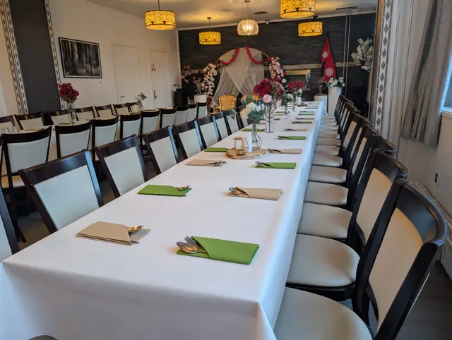 A long white table with green and kraft napkins over the cutlery, red and pink roses in vases, and a white draped floral canopy at the far end