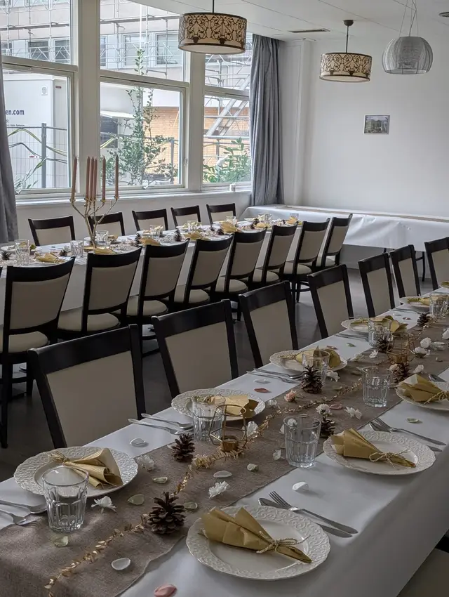 Daylight through tall windows onto two long tables with pale yellow napkins, pine cones and petals on a jute runner