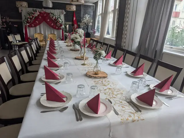 Long white banquet table with raspberry napkins and wood-slice centrepieces, leading to two gilded chairs on a red draped backdrop