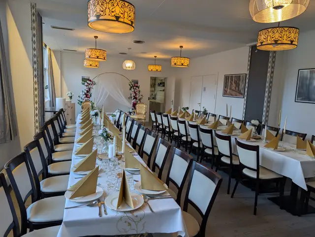 Long tables in white and gold with cone-folded gold napkins and tall candles, facing a white draped arch with pink and red flowers