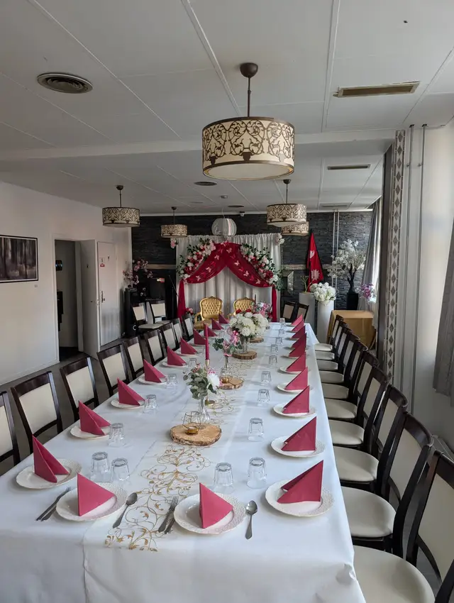 A long table in raspberry and white towards two gilded chairs, wood slice centrepieces, dark stone wall, lit pendants