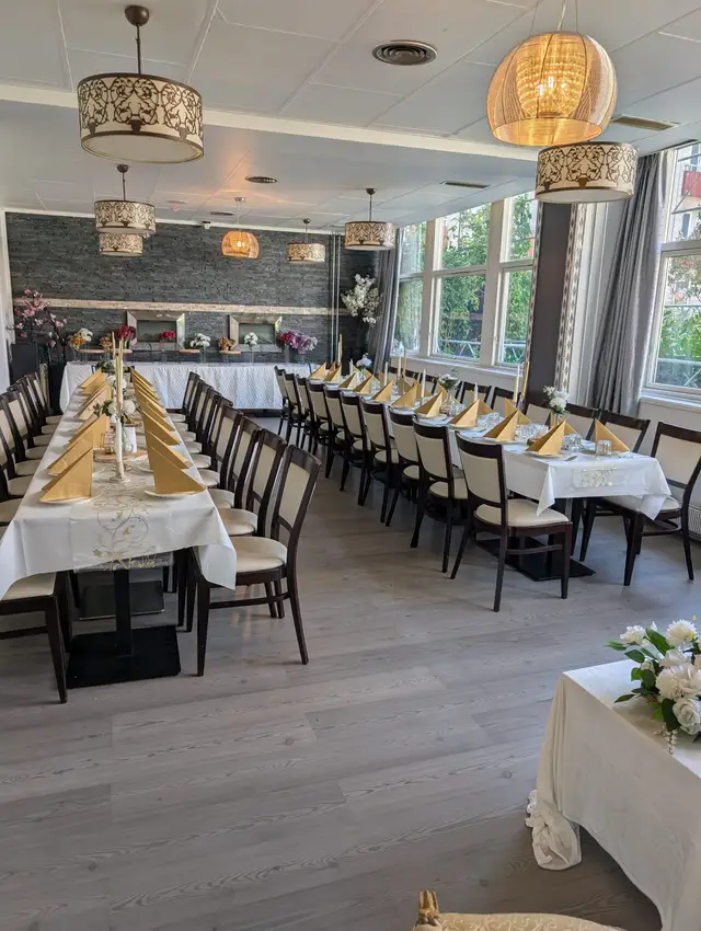 Daylight on two long tables with cream cloths and gold fan napkins, gold taper candles, and a buffet along the dark stone wall behind