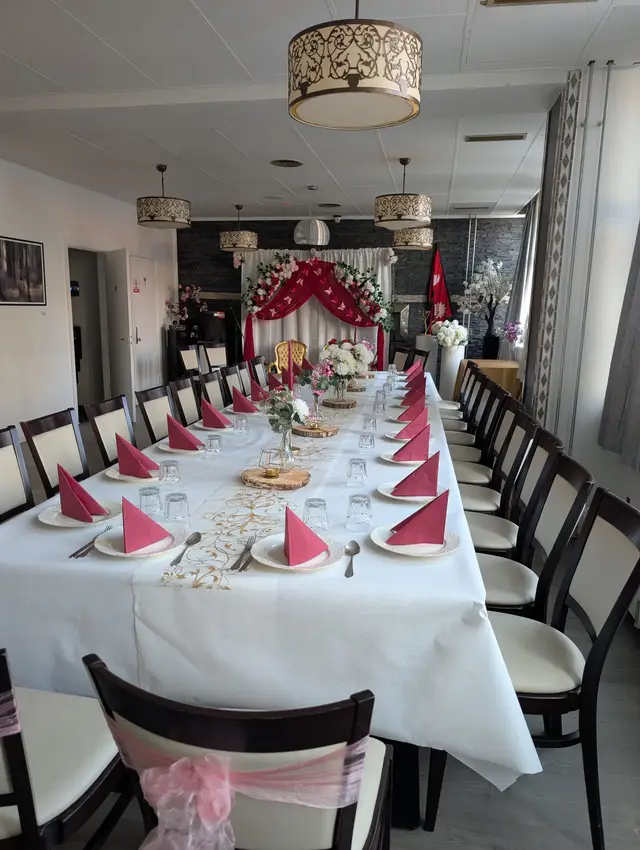 Long table with raspberry napkins and white hydrangeas, pink organza sashes on the near chairs, red draped backdrop at the far end
