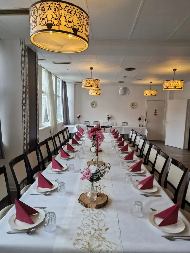 Bright hall in daylight: a long table with raspberry napkins and pink roses on wood slices, smaller tables set at the far end
