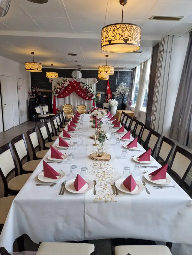 The hall seen down one long table of raspberry napkins to two gilded chairs under a red and white draped backdrop