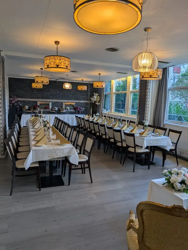 Two long tables laid with white cloths and gold fan napkins, a buffet counter along the dark stone wall, lit pendant lamps above