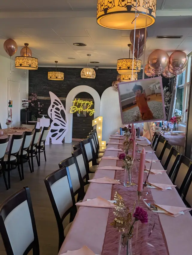 A long table in blush pink with napkins, candles and dried stems, a framed photo of a toddler, rose gold balloons and a neon Happy Birthday sign